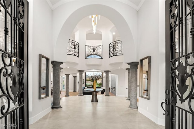 entryway featuring ornamental molding, a towering ceiling, and ornate columns