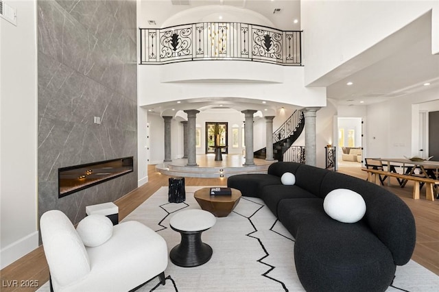 living room with decorative columns, a high ceiling, a high end fireplace, and light hardwood / wood-style floors