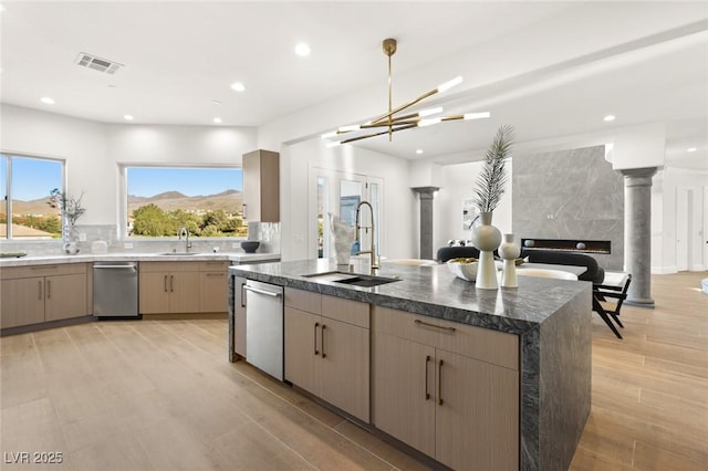 kitchen featuring sink, light brown cabinets, dishwasher, and an island with sink