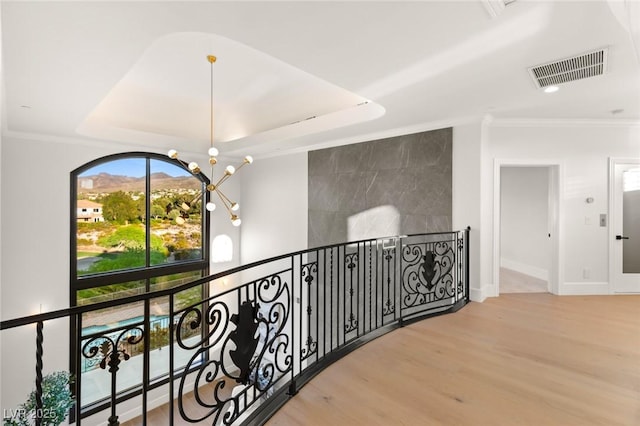 hallway featuring a chandelier, a raised ceiling, ornamental molding, and wood-type flooring