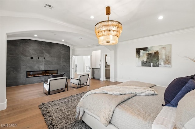 bedroom with a fireplace, wood-type flooring, an inviting chandelier, ornamental molding, and vaulted ceiling