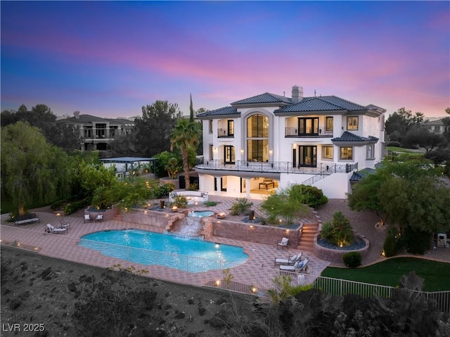 back house at dusk featuring a balcony, a patio area, and a swimming pool with hot tub