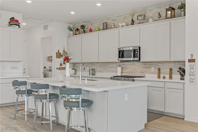 kitchen with white cabinets, a kitchen island with sink, stove, and sink