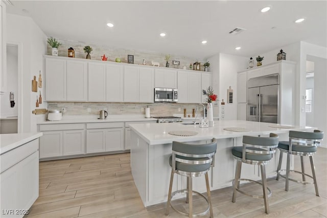 kitchen with a kitchen island with sink, a kitchen breakfast bar, white cabinets, sink, and stainless steel appliances