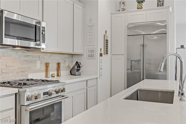 kitchen featuring sink, backsplash, white cabinets, and high end appliances