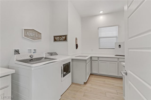 laundry room with washer and clothes dryer, light hardwood / wood-style flooring, and cabinets