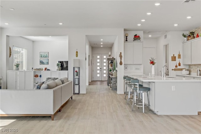 kitchen with a large island with sink, white cabinets, french doors, light hardwood / wood-style floors, and sink