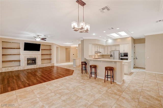 kitchen with pendant lighting, stainless steel refrigerator with ice dispenser, a kitchen bar, built in features, and kitchen peninsula