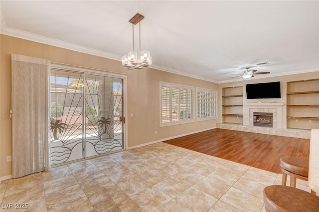 unfurnished living room with ceiling fan with notable chandelier, built in shelves, wood-type flooring, a fireplace, and crown molding