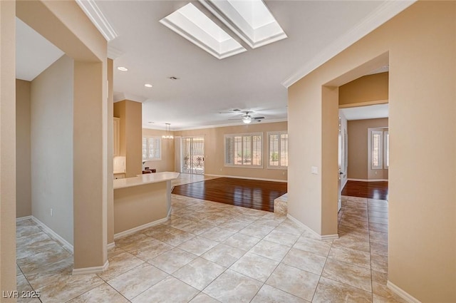 kitchen with ceiling fan with notable chandelier, a skylight, light tile patterned floors, and crown molding