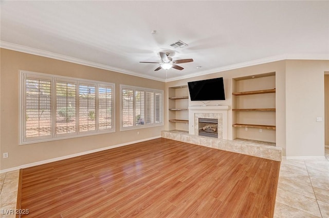 unfurnished living room with ceiling fan, a wealth of natural light, built in features, and a premium fireplace