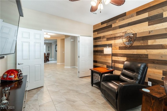 living area featuring ceiling fan and wooden walls