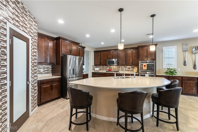 kitchen with appliances with stainless steel finishes, sink, decorative light fixtures, an island with sink, and decorative backsplash