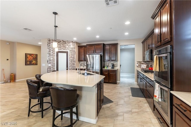 kitchen with pendant lighting, appliances with stainless steel finishes, sink, tasteful backsplash, and an island with sink