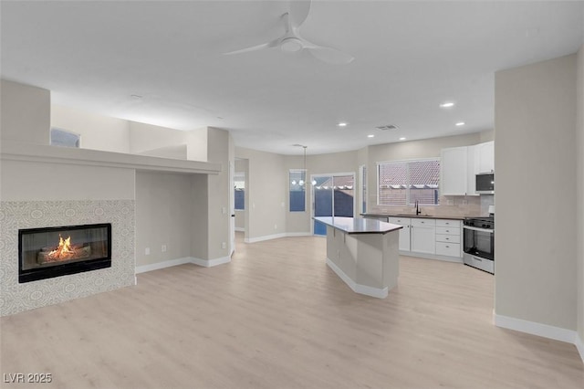 kitchen with light hardwood / wood-style flooring, white cabinetry, stainless steel gas stove, backsplash, and a tile fireplace