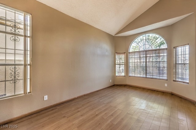 unfurnished room with light wood-type flooring, a textured ceiling, and vaulted ceiling