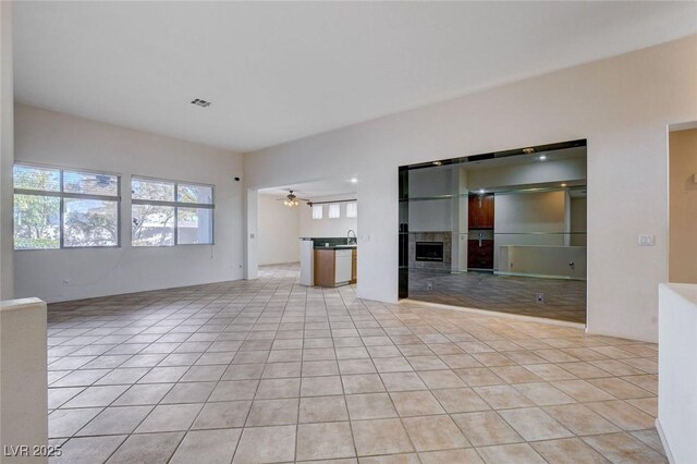 unfurnished living room featuring a tile fireplace, ceiling fan, and light tile patterned flooring