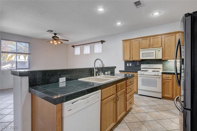 kitchen with sink, backsplash, light tile patterned floors, white appliances, and a center island with sink