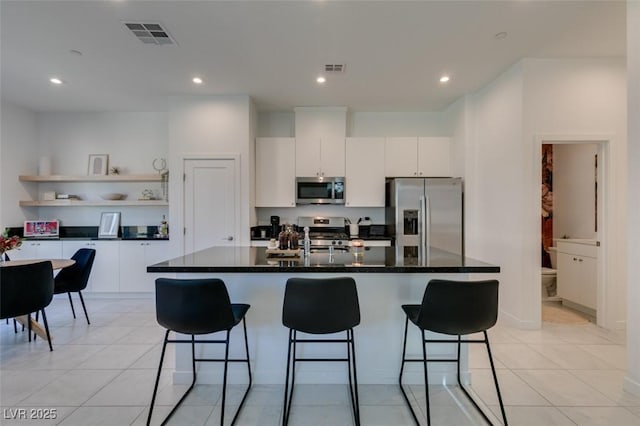 kitchen with light tile patterned floors, white cabinetry, appliances with stainless steel finishes, and a center island with sink