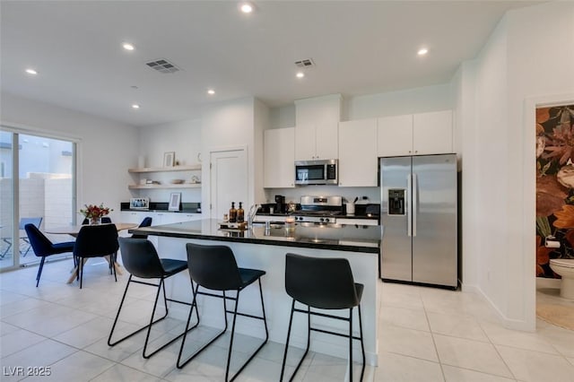 kitchen with appliances with stainless steel finishes, white cabinetry, light tile patterned floors, an island with sink, and a breakfast bar area