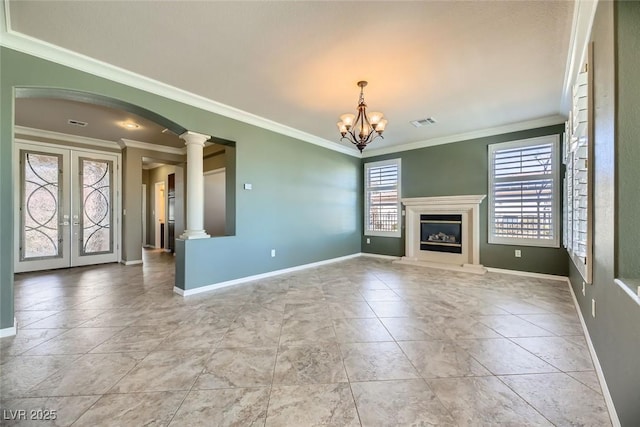 unfurnished living room featuring ornate columns, ornamental molding, french doors, and an inviting chandelier