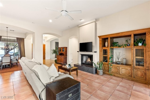 living room featuring a fireplace, ceiling fan with notable chandelier, and light tile patterned floors