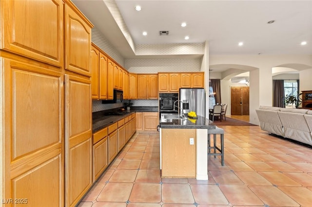 kitchen with black appliances, a kitchen bar, a kitchen island with sink, decorative backsplash, and sink