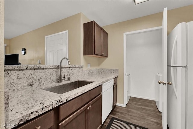 kitchen with light stone countertops, white appliances, dark wood-type flooring, sink, and dark brown cabinets