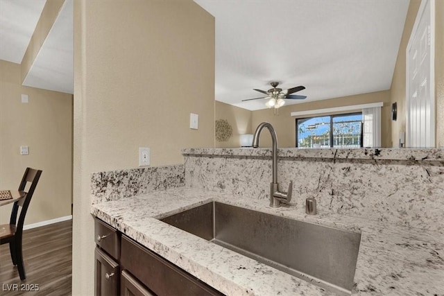 kitchen featuring sink, dark brown cabinetry, ceiling fan, light stone counters, and dark hardwood / wood-style floors