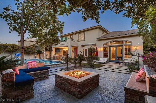 back house at dusk featuring french doors, a balcony, a patio area, and a fire pit