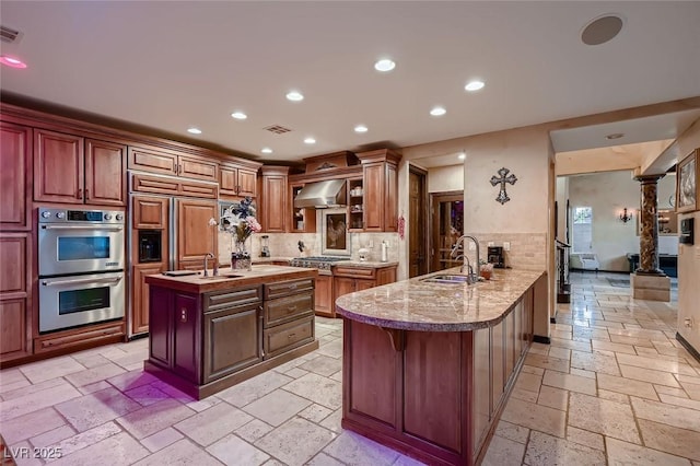 kitchen with sink, wall chimney range hood, a breakfast bar, appliances with stainless steel finishes, and kitchen peninsula