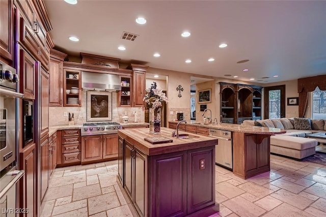 kitchen with sink, a breakfast bar area, butcher block countertops, appliances with stainless steel finishes, and an island with sink