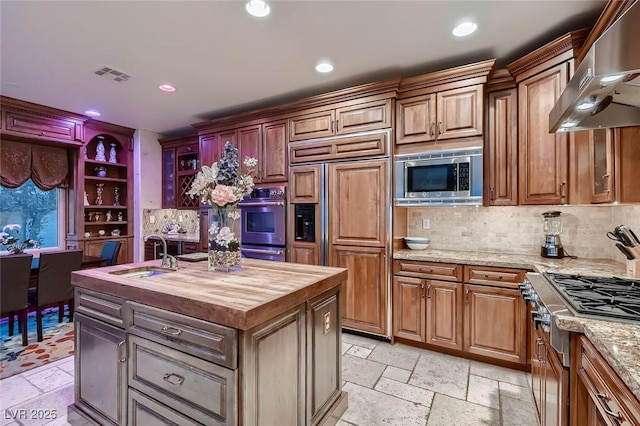 kitchen featuring butcher block countertops, sink, built in appliances, extractor fan, and a center island with sink