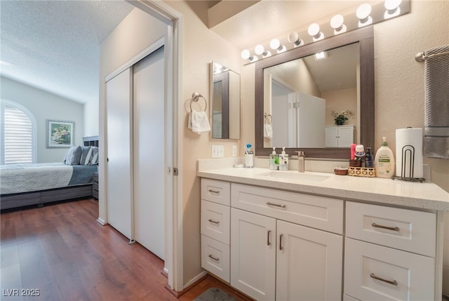 bathroom featuring hardwood / wood-style flooring, a textured ceiling, vanity, and lofted ceiling