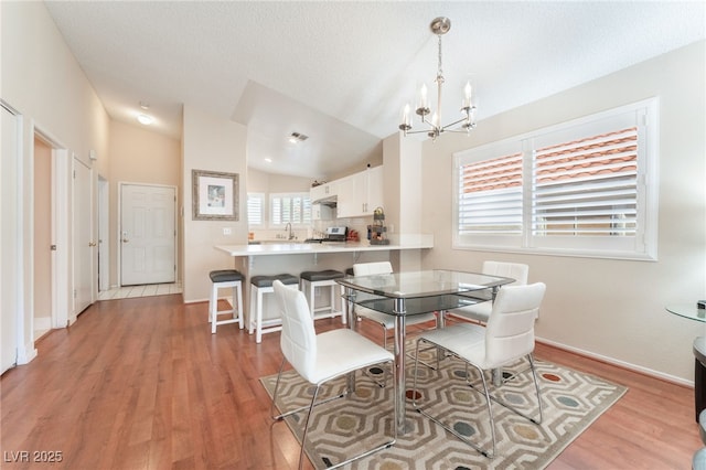 dining area featuring sink, a healthy amount of sunlight, light hardwood / wood-style flooring, and lofted ceiling