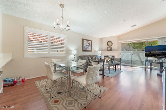 dining room with hardwood / wood-style floors, a chandelier, a textured ceiling, and vaulted ceiling