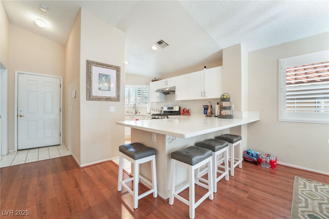 kitchen featuring kitchen peninsula, vaulted ceiling, stainless steel stove, white cabinets, and a textured ceiling