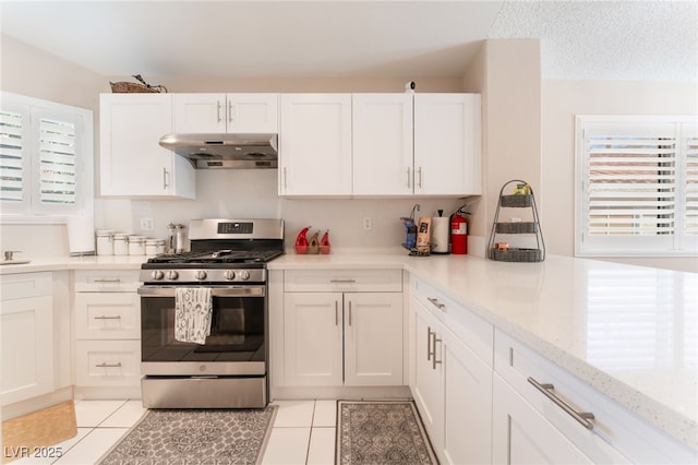 kitchen with white cabinetry, stainless steel gas range, light tile patterned floors, and light stone counters