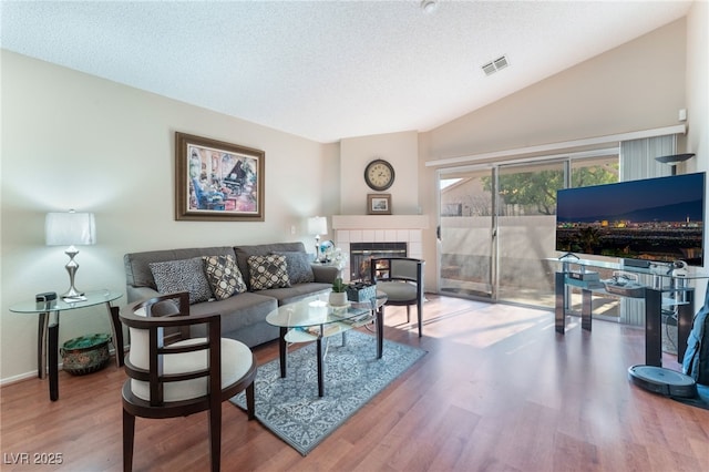 living room with a textured ceiling, lofted ceiling, hardwood / wood-style floors, and a fireplace