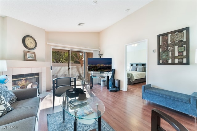 living room featuring vaulted ceiling, hardwood / wood-style floors, a textured ceiling, and a tiled fireplace