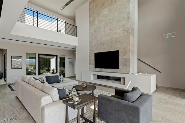 living room featuring a towering ceiling, baseboards, a premium fireplace, and visible vents