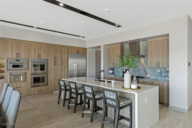 kitchen featuring light countertops, appliances with stainless steel finishes, a kitchen island with sink, a sink, and modern cabinets