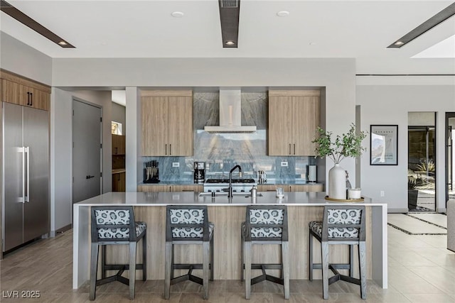 kitchen with built in fridge, a kitchen breakfast bar, light countertops, wall chimney range hood, and modern cabinets