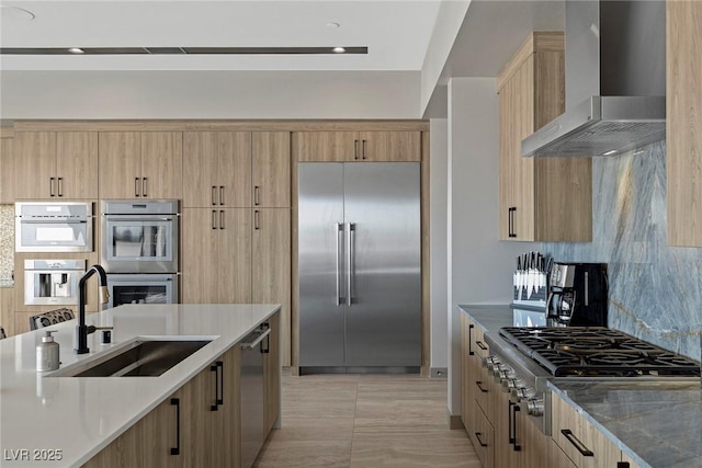 kitchen featuring stainless steel appliances, tasteful backsplash, a sink, dark stone countertops, and wall chimney exhaust hood