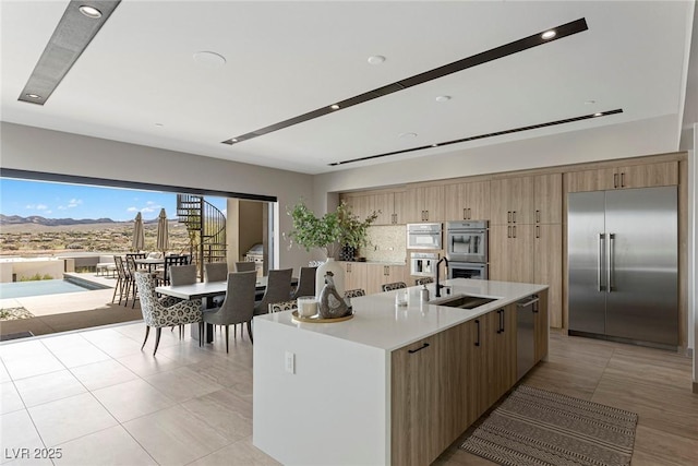 kitchen featuring a center island with sink, stainless steel appliances, light countertops, backsplash, and a sink