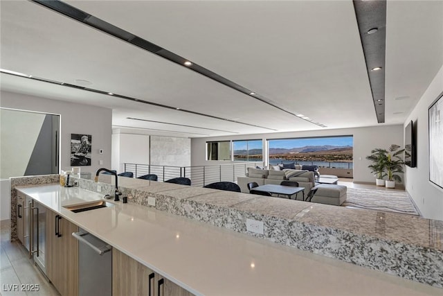 kitchen with open floor plan, light brown cabinets, a sink, and light stone countertops