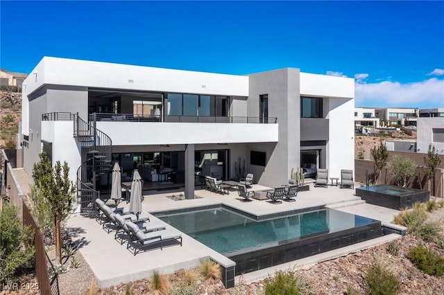 rear view of property featuring a hot tub, stairway, an infinity pool, a patio area, and stucco siding