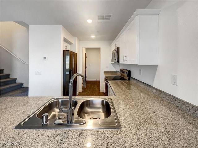 kitchen with black refrigerator, white cabinets, sink, electric range, and light stone counters