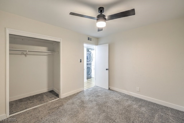 unfurnished bedroom featuring a closet, ceiling fan, carpet flooring, and stacked washer / dryer