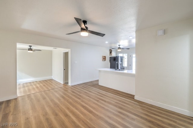 unfurnished living room with ceiling fan, sink, wood-type flooring, and a textured ceiling